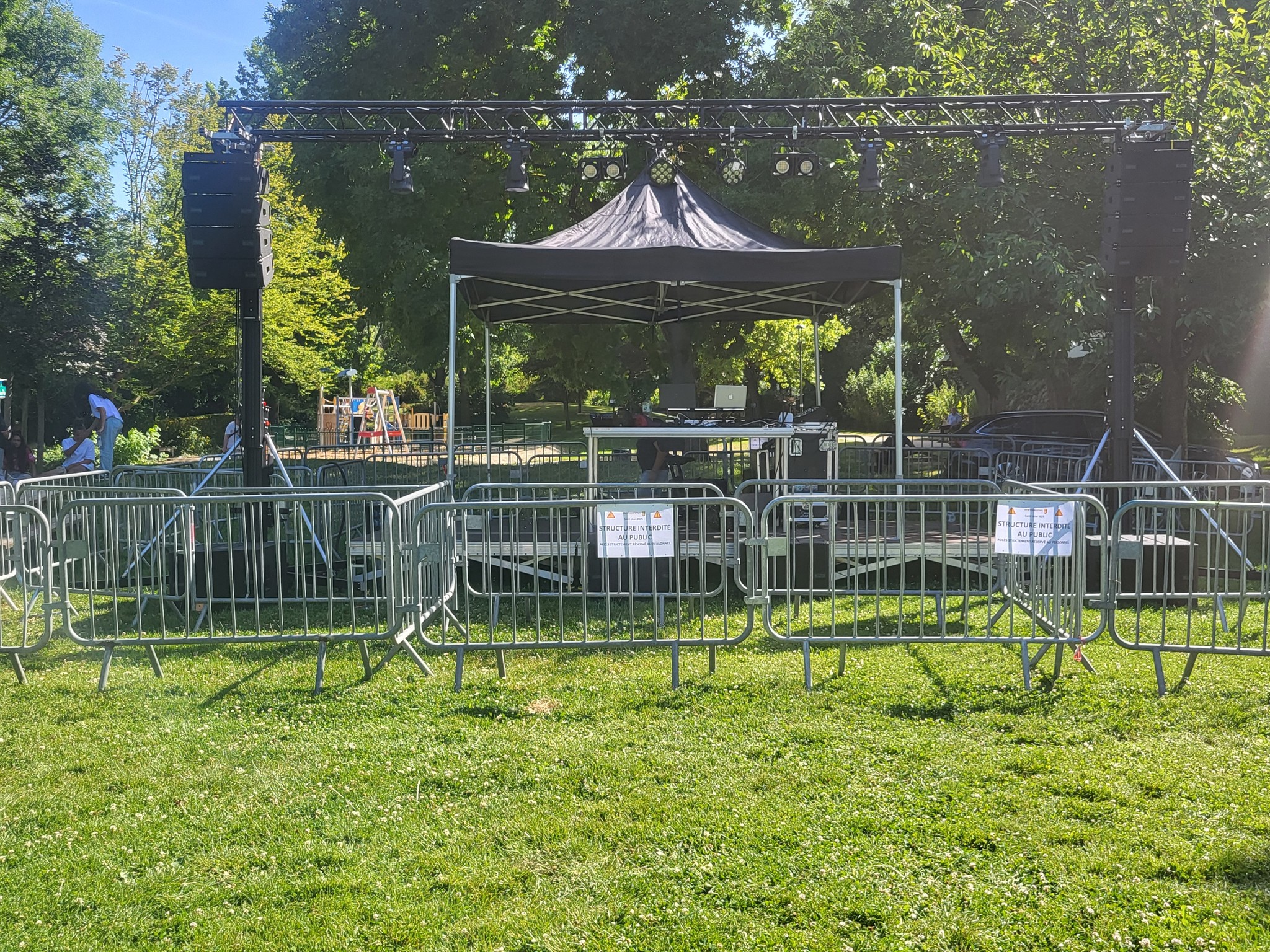 Installation de sono et éclairage sous un chapiteau, entourée de barrières sur un terrain gazonné, prête pour un événement.