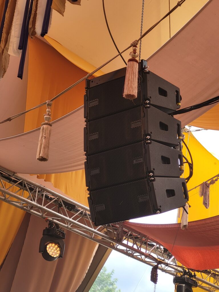 Système de sonorisation suspendu, installé sous une structure colorée, pour un événement.