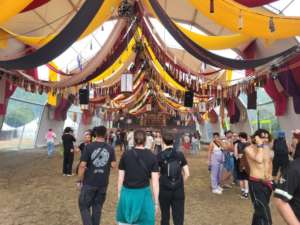 Installation de matériel de sono et éclairage dans une tente lors d'un festival, avec un public rassemblé.