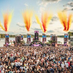 Une foule enthousiaste lors d'un événement festif en plein air, avec un grand podium et des effets pyrotechniques colorés.