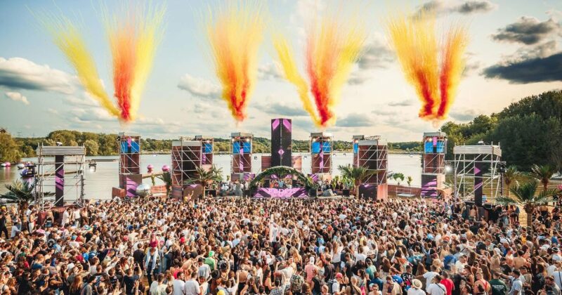 Une foule enthousiaste lors d'un événement festif en plein air, avec un grand podium et des effets pyrotechniques colorés.