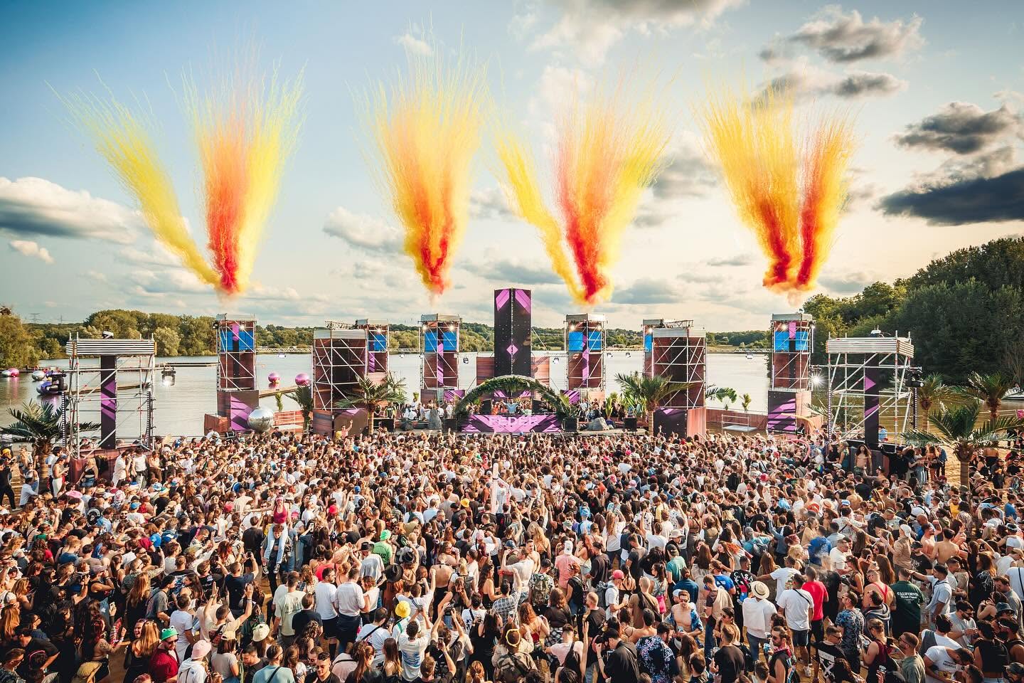 Une foule enthousiaste lors d'un événement festif en plein air, avec un grand podium et des effets pyrotechniques colorés.