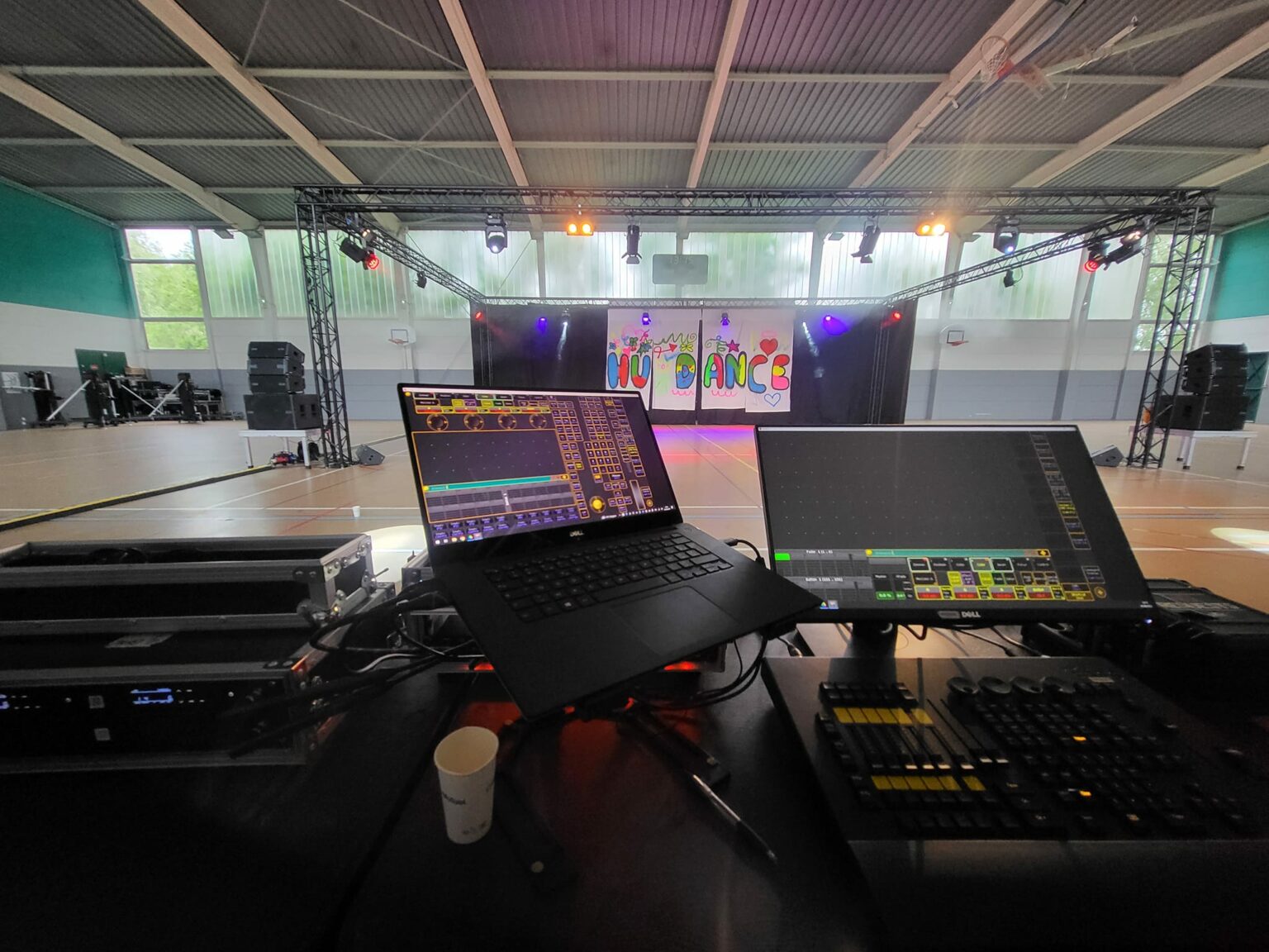 Vue du matériel de son et lumière pour un événement, avec des écrans de contrôle et une scène éclairée en arrière-plan.