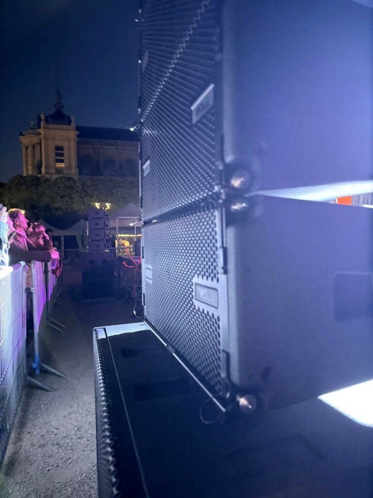 Équipements de sonorisation en pleine installation lors d'un événement nocturne, avec un public en arrière-plan.
