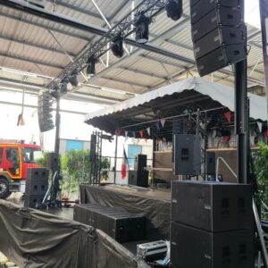 Installation de matériel de son et éclairage sur scène en préparation d'un événement, avec structures et équipements visibles.