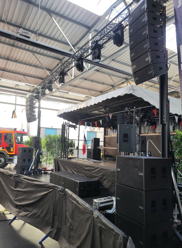 Installation de matériel de son et éclairage sur scène en préparation d'un événement, avec structures et équipements visibles.