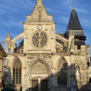 Église ancienne avec une façade en pierre, vitraux et horloge, sous un ciel bleu.