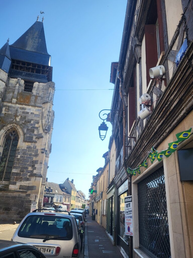 Rue animée avec bâtiments anciens, équipement sonore visible, ciel bleu clair.