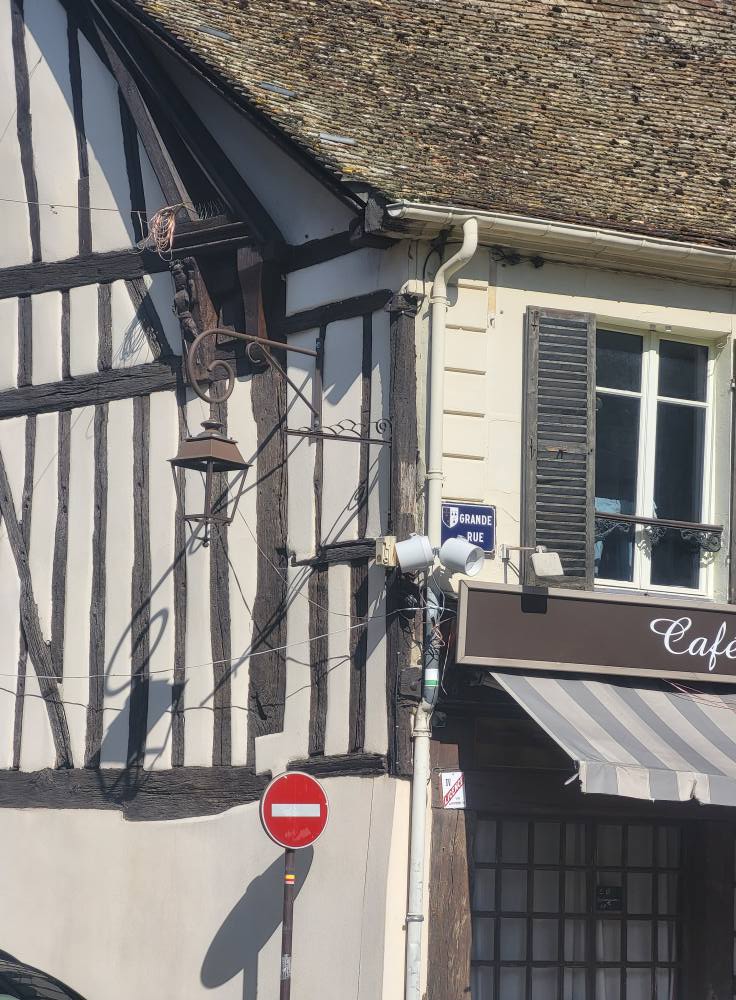 Façade en bois traditionnel avec un panneau de rue et un café, devant un mur à colombages.