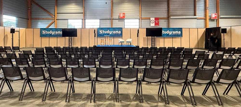 Salle de conférence avec rangées de chaises, podium et écrans pour un événement Studyrama.