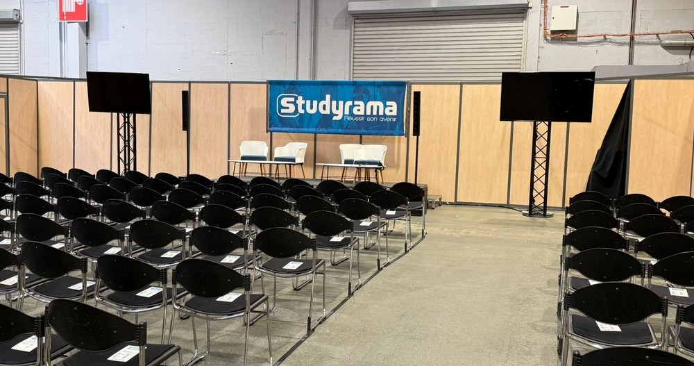Salle de conférence avec chaises en rangées, podium, écran et bannière "Studyrama".