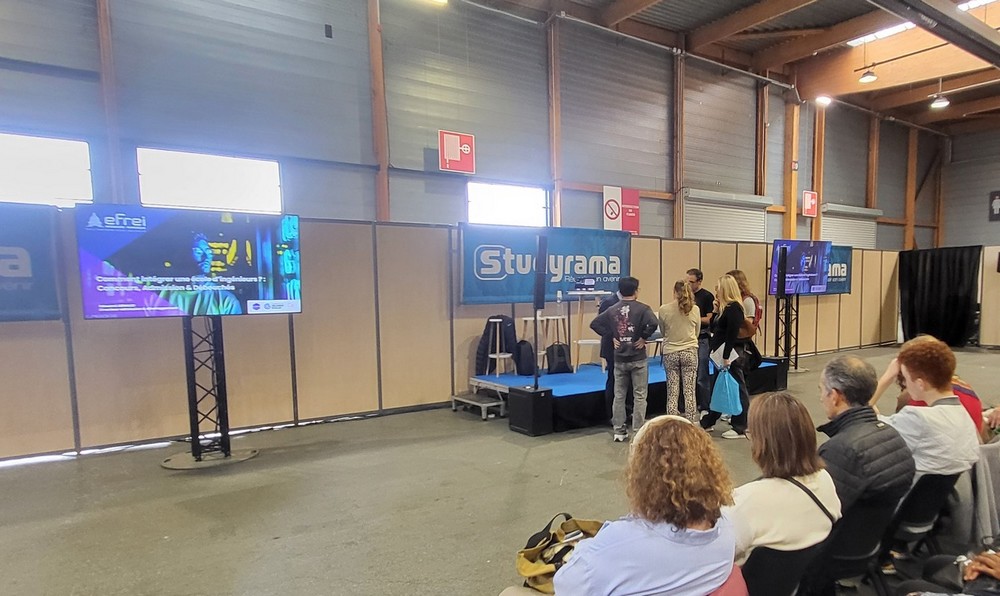 Stand de Symbiose Organisation présentant du matériel de sono et éclairage lors d'un événement, avec des visiteurs attentifs.