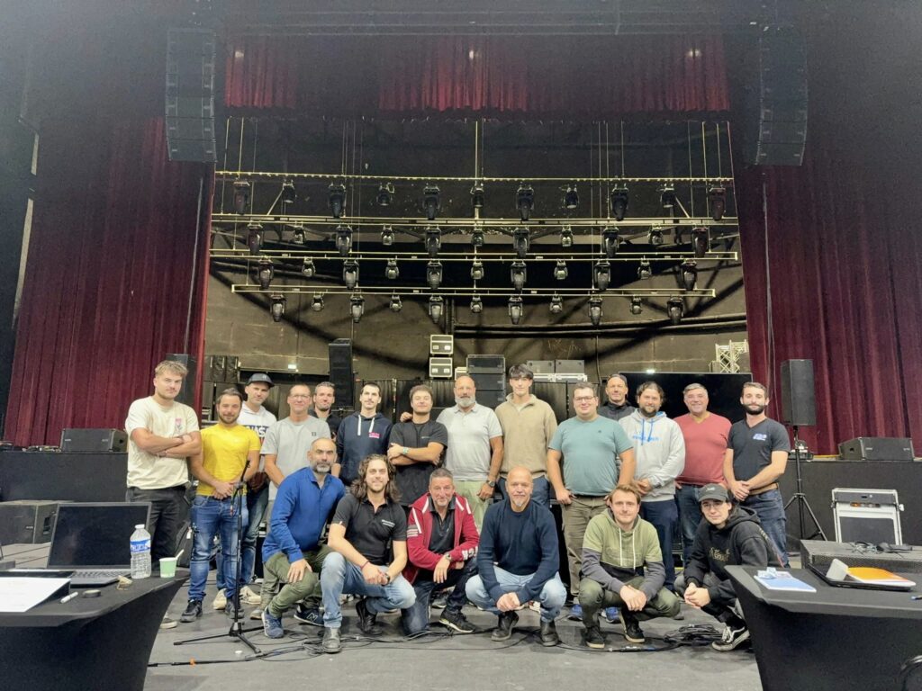 Équipe de Symbiose Organisation réunie sur scène, entourée de matériel de son et d'éclairage lors d'une installation.
