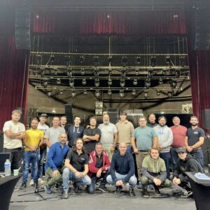 Équipe de Symbiose Organisation réunie sur scène, entourée de matériel de son et d'éclairage lors d'une installation.