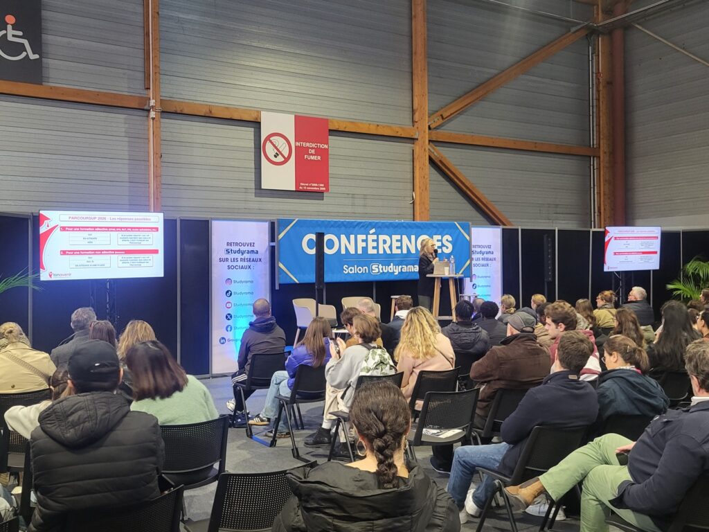 Conférence au Salon Studyrama avec un intervenant et un public attentif, décor et matériel de sonorisation visibles.
