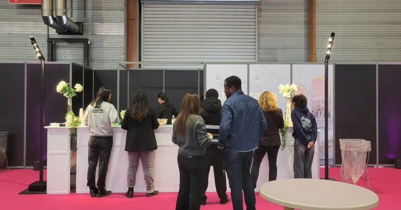Groupe de personnes au comptoir d'un événement, attendant avec des éléments de décoration florale en arrière-plan.