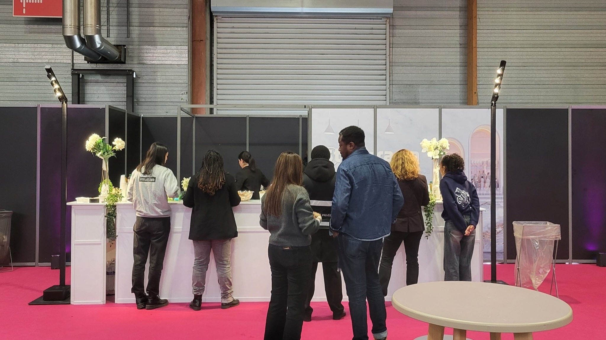 Groupe de personnes au comptoir d'un événement, attendant avec des éléments de décoration florale en arrière-plan.