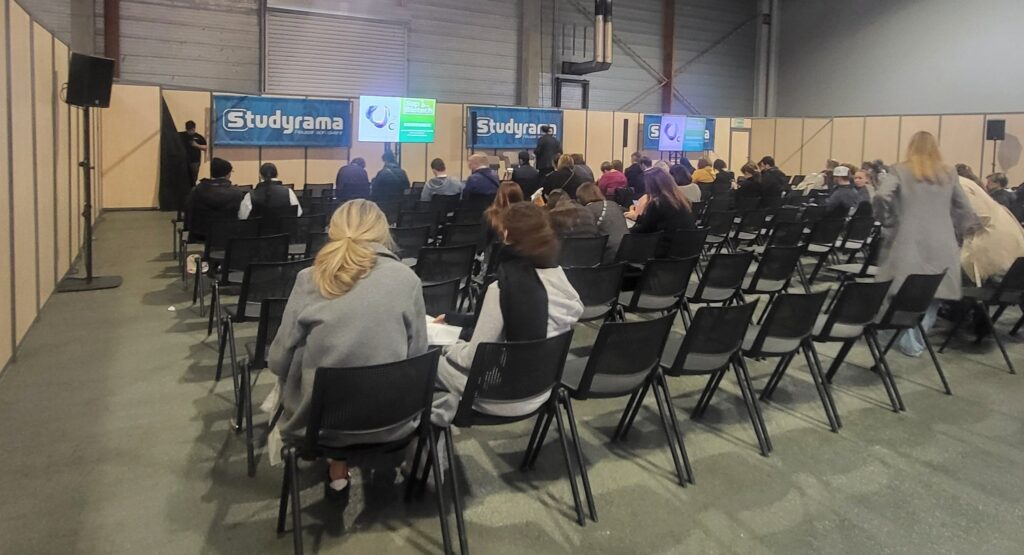 Salle de conférence avec des chaises vides, panneaux "Studyrama" en arrière-plan et participants en attente.