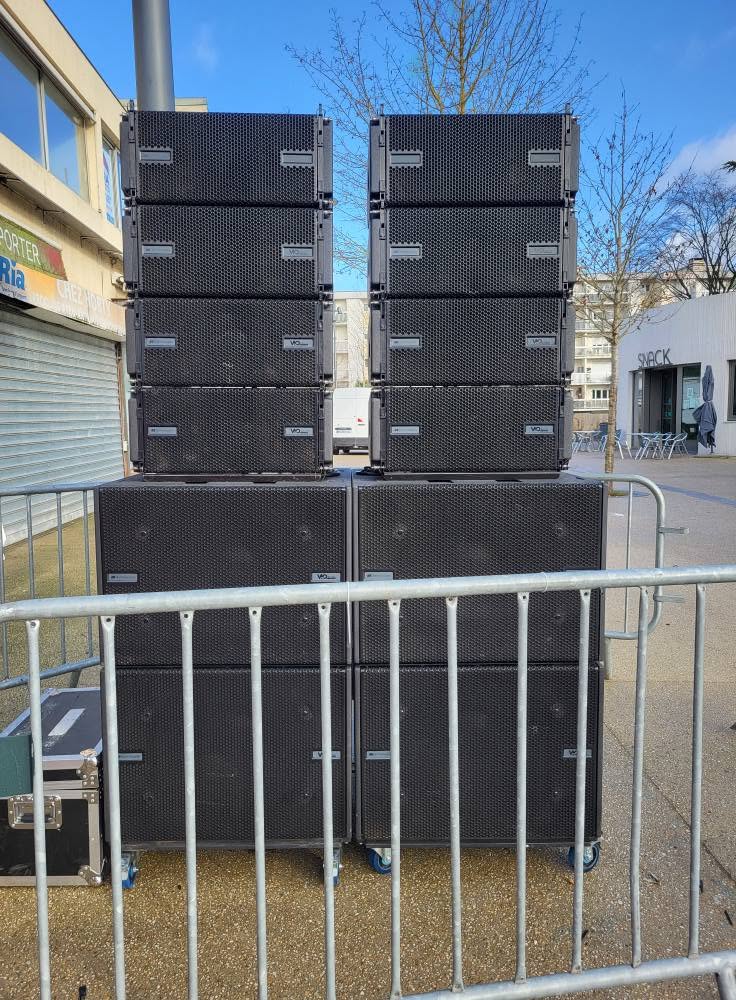 Système de sonorisation empilé, prêt pour un événement en extérieur, avec barrières de sécurité autour.