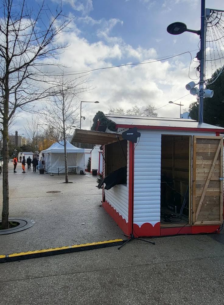 Stands de marché avec matériel de sono et éclairage en préparation, sous un ciel nuageux.