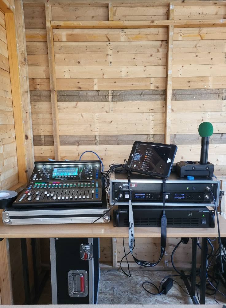 Équipement de sonorisation et de contrôle audio dans un espace en bois. Console de mixage, ordinateurs et matériel connecté.