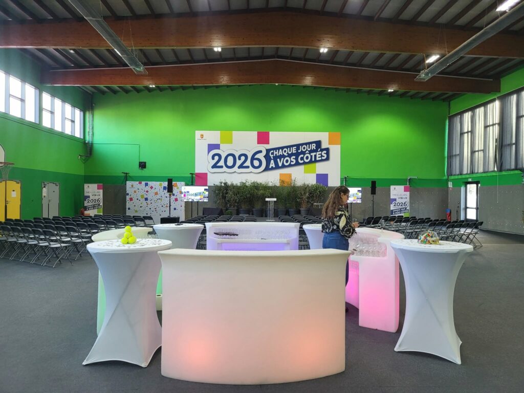Événement dans un gymnase avec tables, chaises et décoration colorée pour 2026, préparations pour une réception.