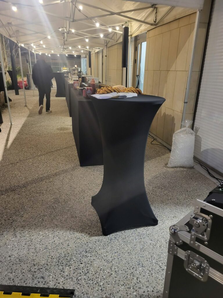 Installation d'un bar avec des boissons et des pâtisseries sous un chapiteau, éclairé par des guirlandes lumineuses.