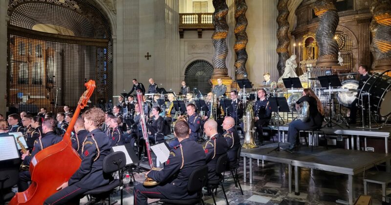 Concert d'un orchestre avec des musiciens en uniforme, dans un cadre architectural majestueux.