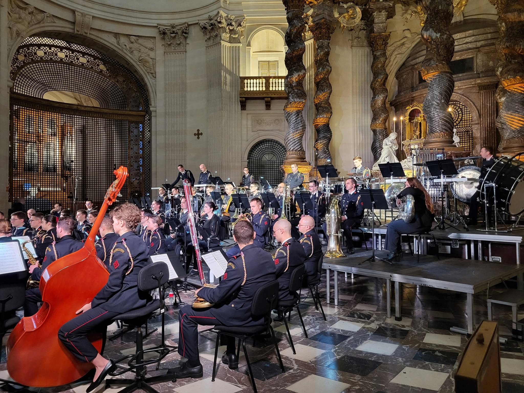 Concert d'un orchestre avec des musiciens en uniforme, dans un cadre architectural majestueux.
