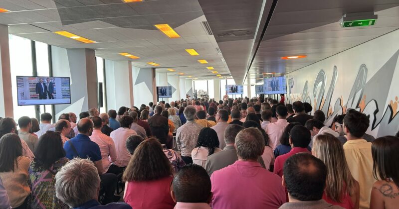 Une foule nombreuse assiste à une présentation dans une salle moderne, avec des écrans affichant des images.