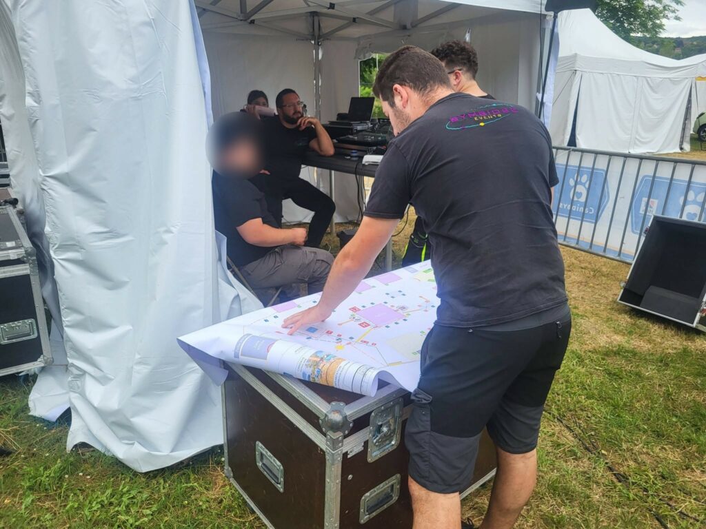 Groupe de techniciens étudiant un plan d'installation de son et éclairage sous un chapiteau pendant un événement.