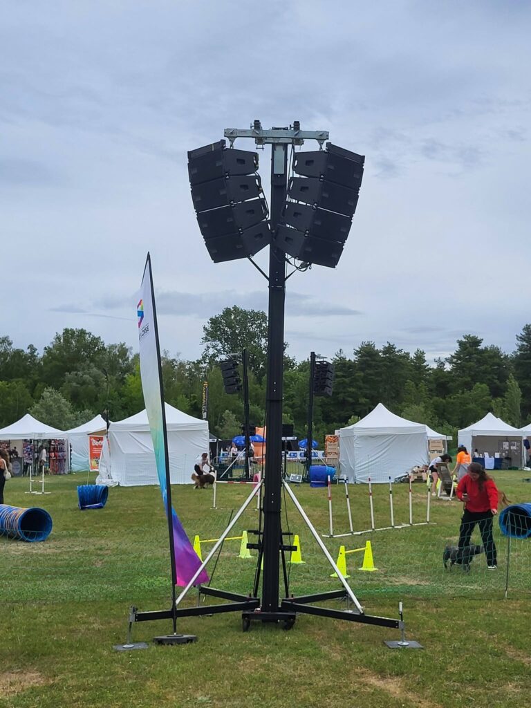 Système de sonorisation installé sur un support, avec des tentes et du matériel pour un événement en plein air.