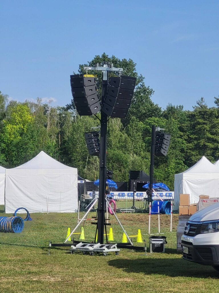 Système de sonorisation installé sur un terrain, entouré de tentes et obstacles, pour un événement en plein air.