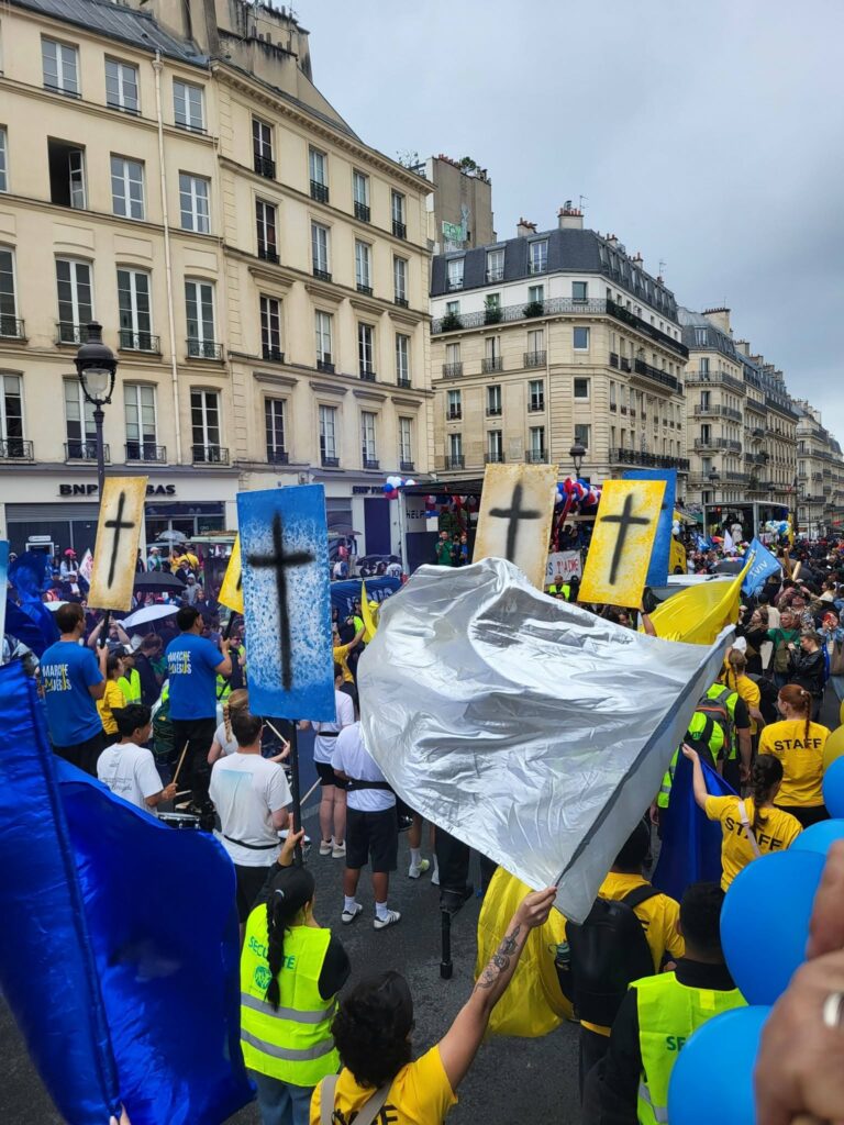 Manifestation animée avec des participants portant des t-shirts jaunes et des drapeaux colorés, dans une rue parisienne.