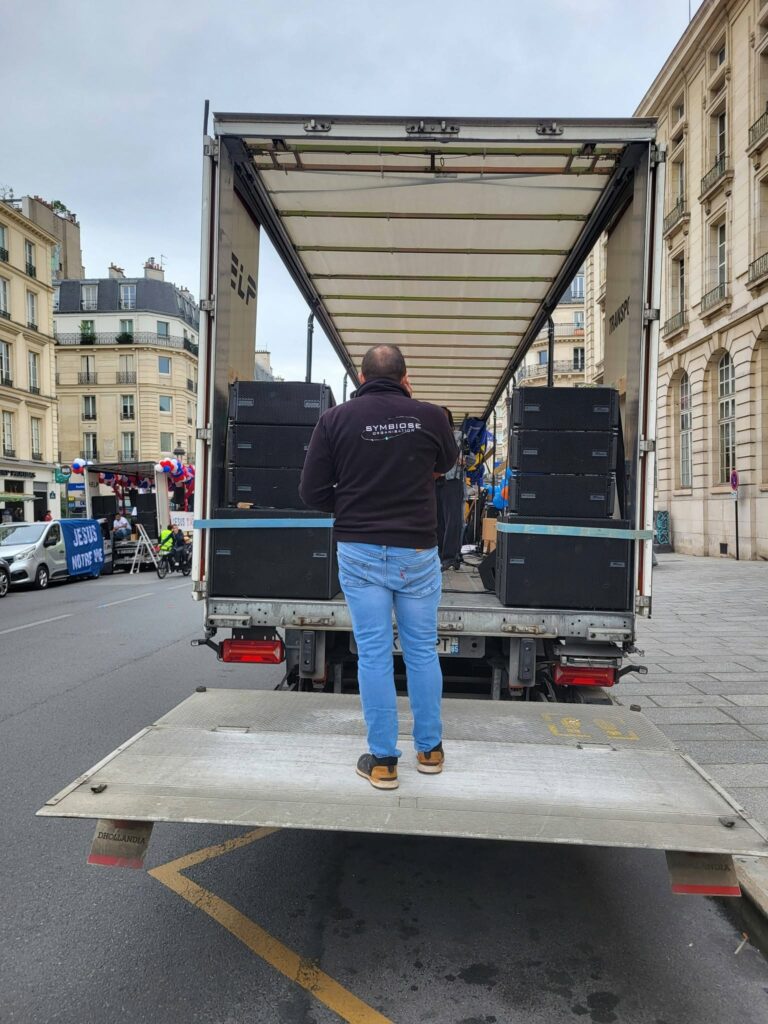 Un technicien de Symbiose Organisation supervise le déchargement de matériel de sono et éclairage depuis un camion.