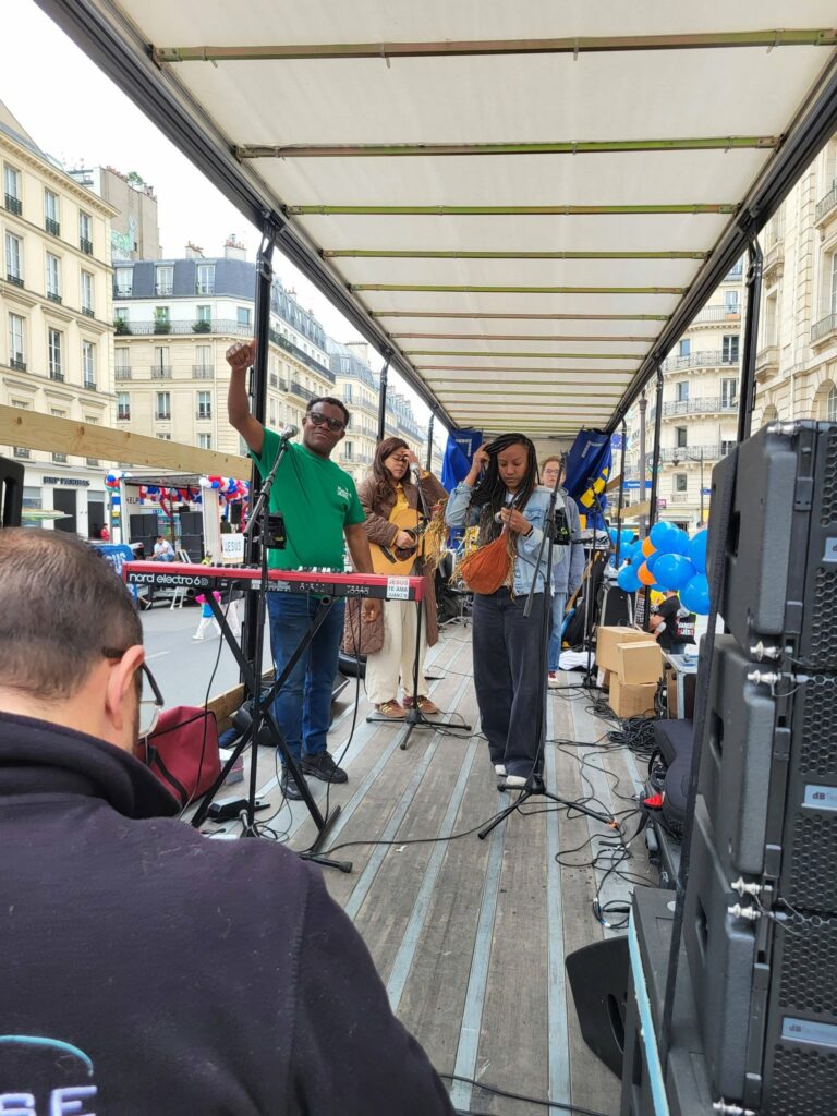 Groupe de musiciens sur scène, avec des instruments, lors d'un événement en extérieur à Paris.