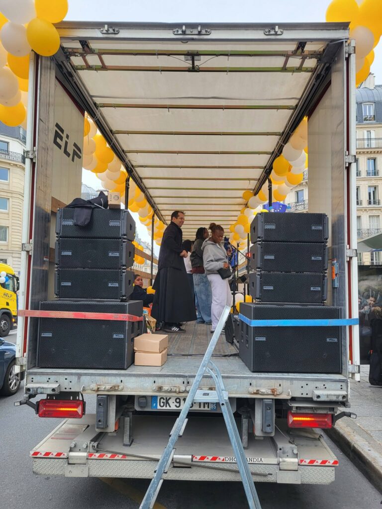 Camion équipé de matériel de sonorisation et éclairage, avec des personnes préparant un événement festif. Ballons jaunes décoratifs.