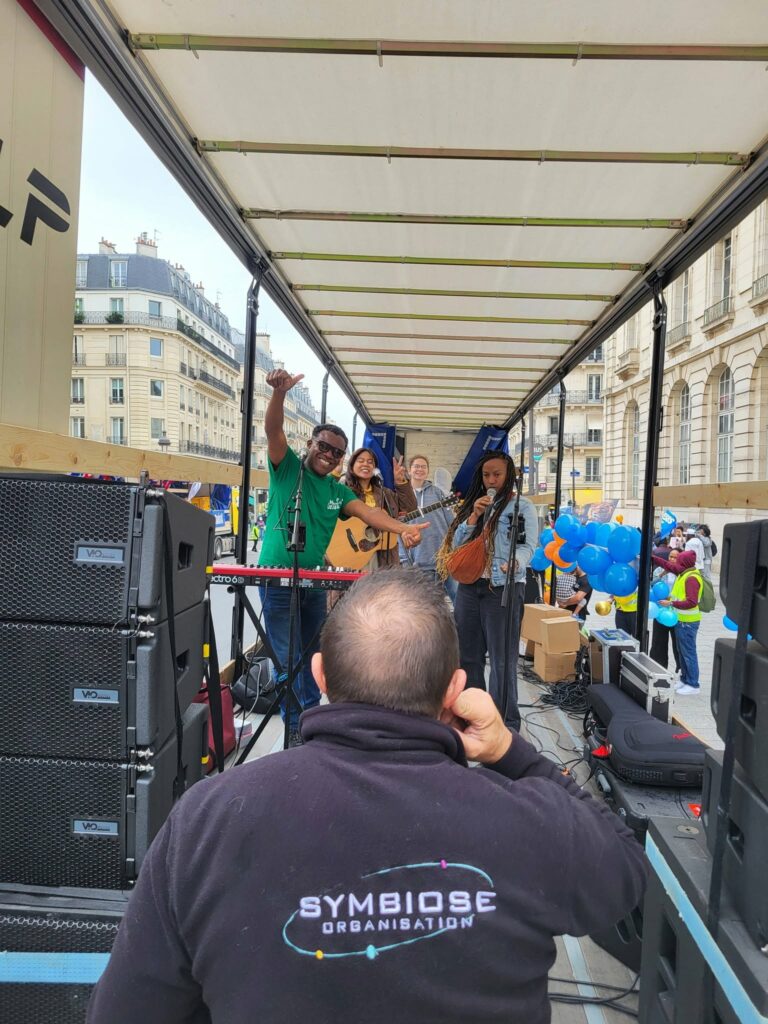 Scène de concert avec des musiciens sur une camionnette, technique de sonorisation en arrière-plan, tenue par Symbiose Organisation.