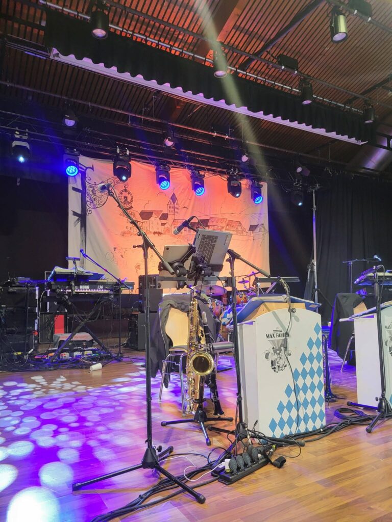 Scène de concert avec matériel de sonorisation et éclairage, saxophone en avant-plan, préparée pour une performance musicale.