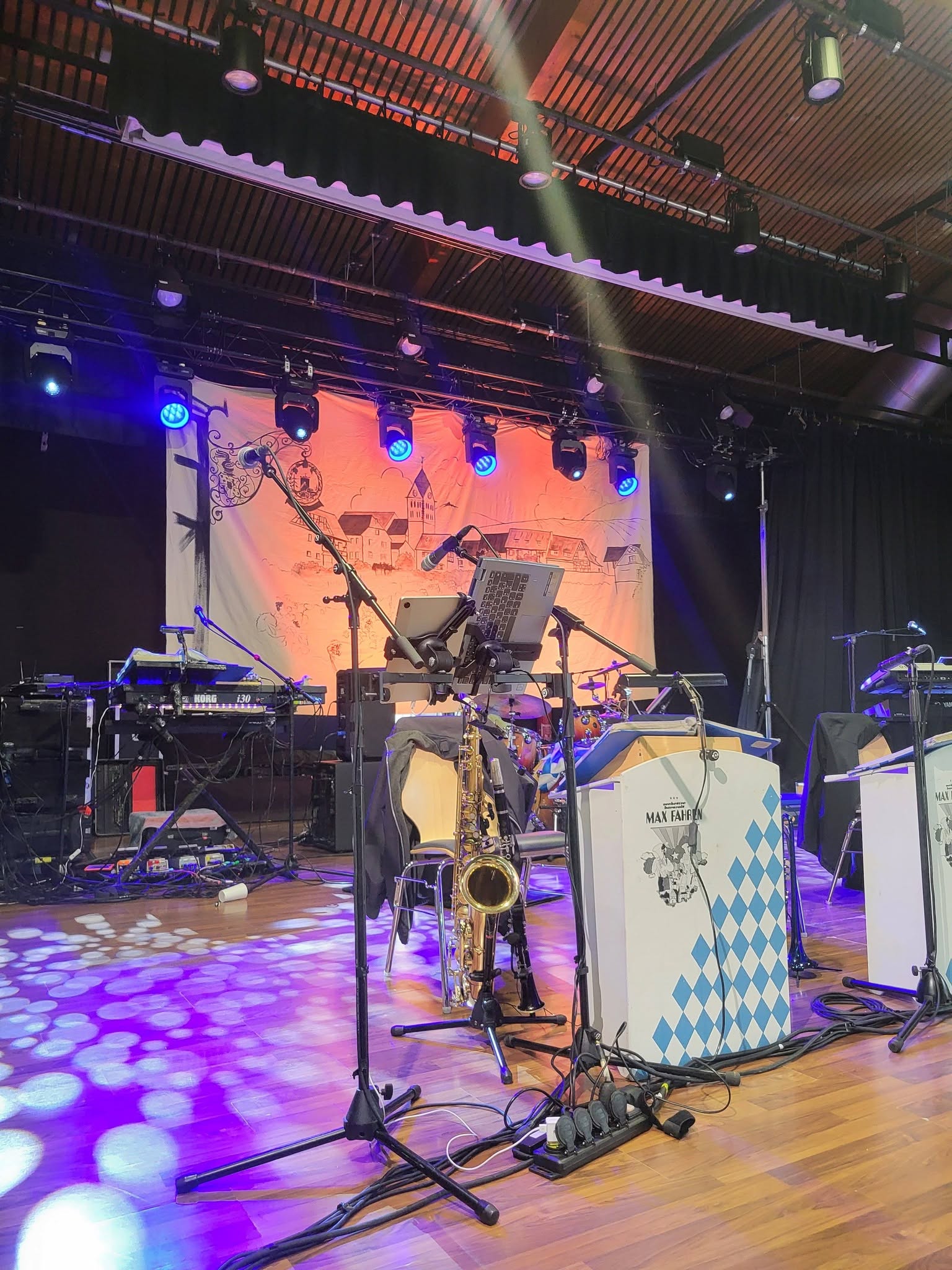 Scène de concert avec matériel de sonorisation et éclairage, saxophone en avant-plan, préparée pour une performance musicale.