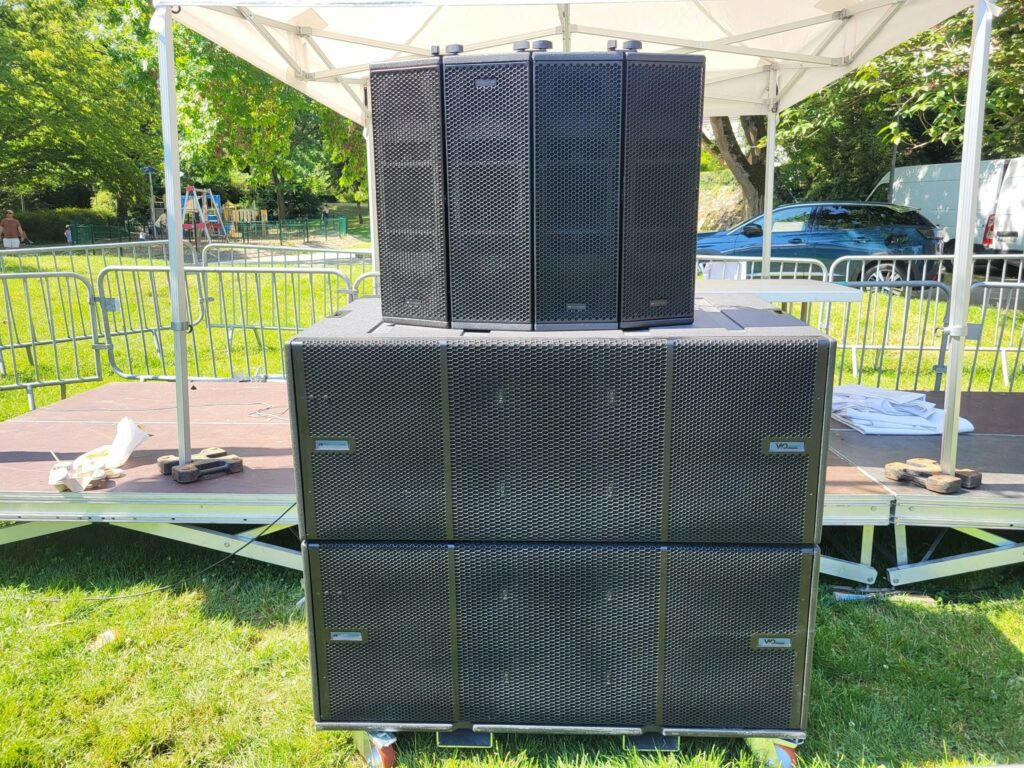 Système de sonorisation installé sur scène, avec plusieurs haut-parleurs en grille noire.