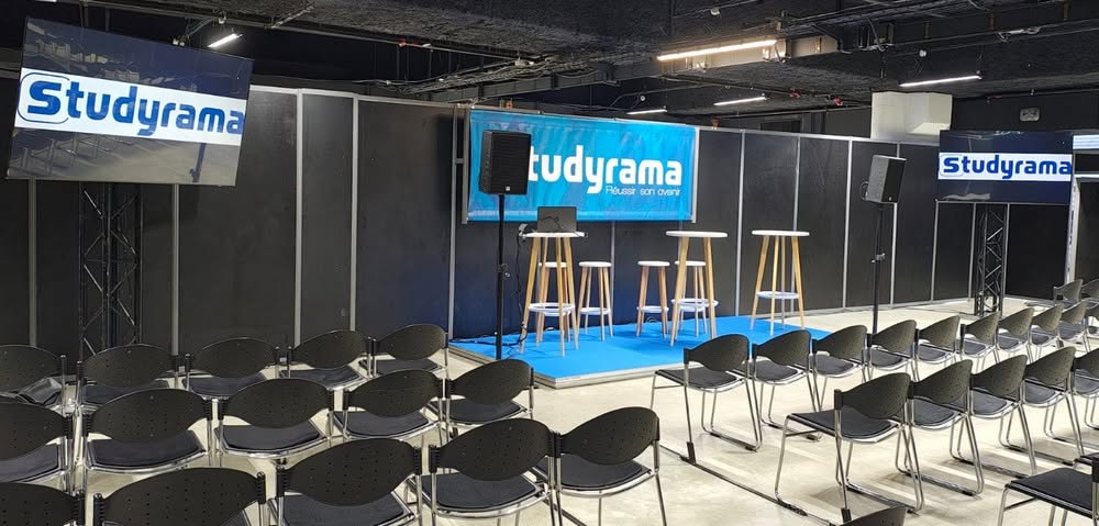 Scène de présentation avec chaises noires, estrades et logos de Studyrama. Préparation pour un événement.