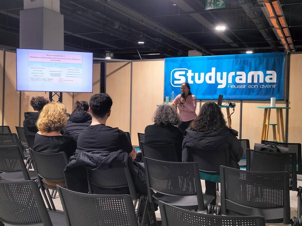 Conférence animée par une intervenante, avec un écran de présentation, devant un public attentif dans un salon professionnel.