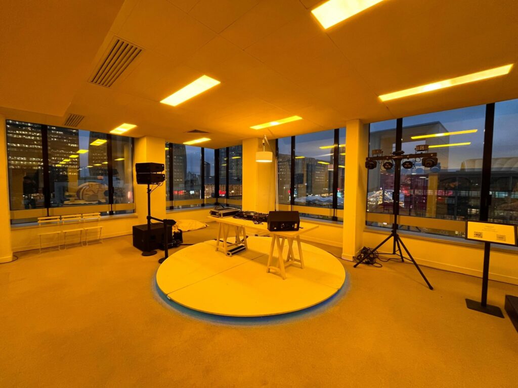 Espace d'événement avec matériel de son et éclairage, fenêtres offrant une vue sur la ville illuminée.