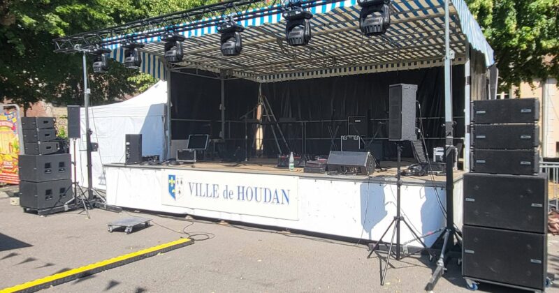 Scène de spectacle équipée de matériel de son et éclairage, ville de Houdan, avec tentes et décorations.