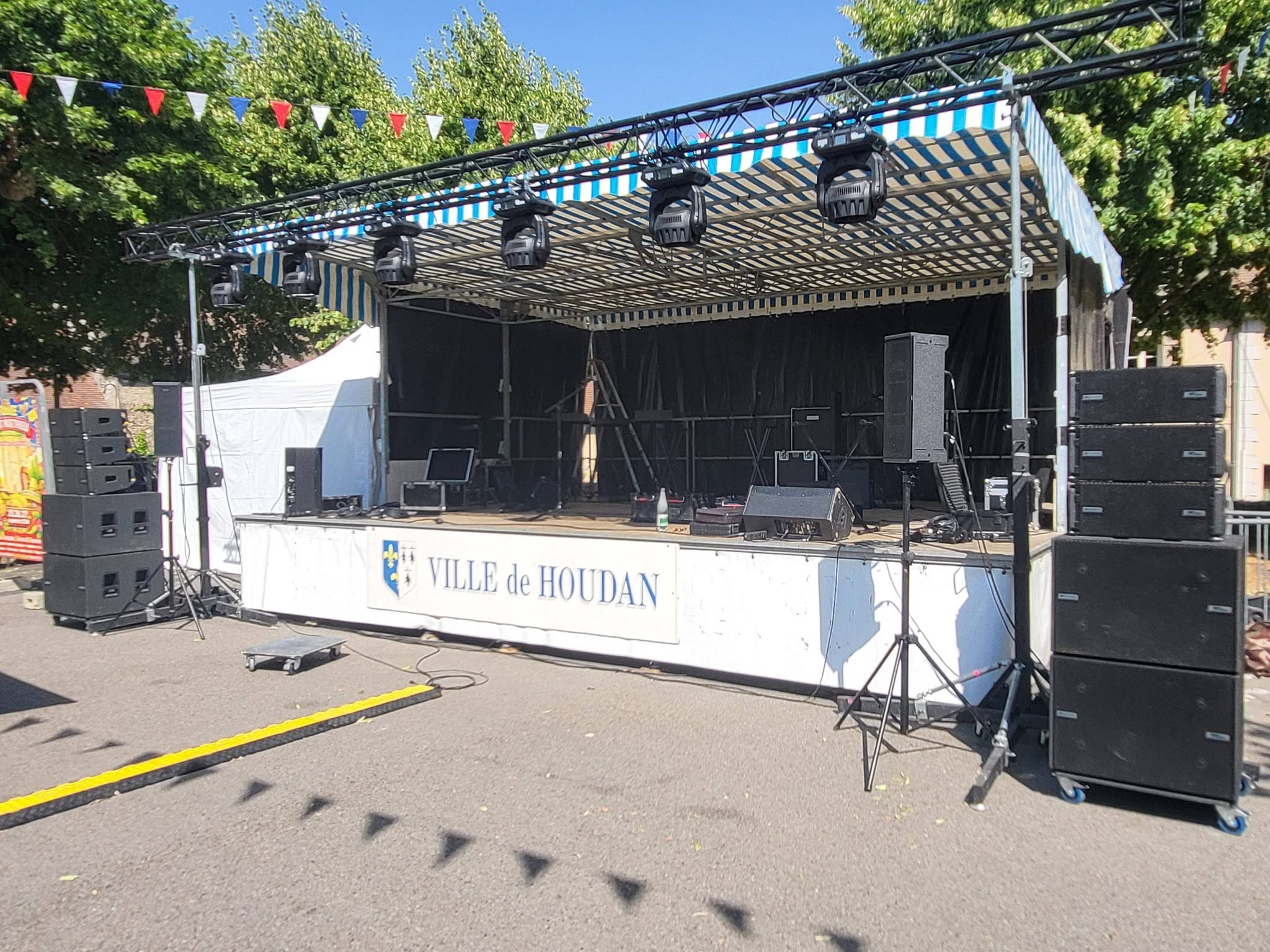 Scène de spectacle équipée de matériel de son et éclairage, ville de Houdan, avec tentes et décorations.