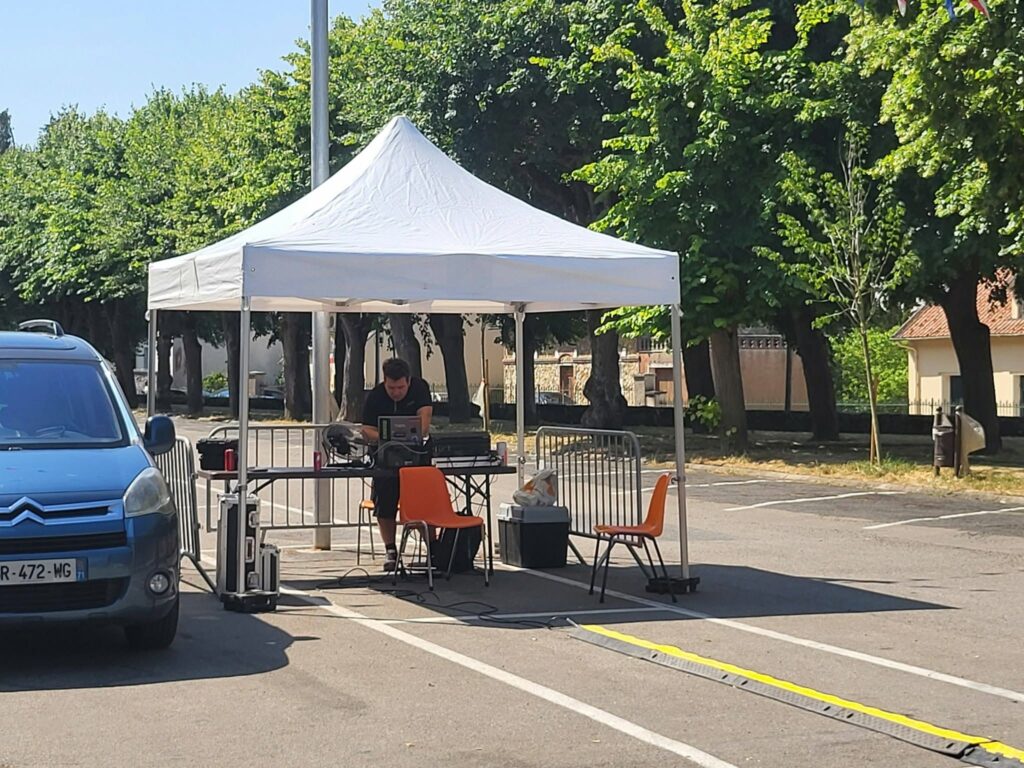 Technicien au travail sous un chapiteau, installant du matériel de sonorisation et éclairage en extérieur.