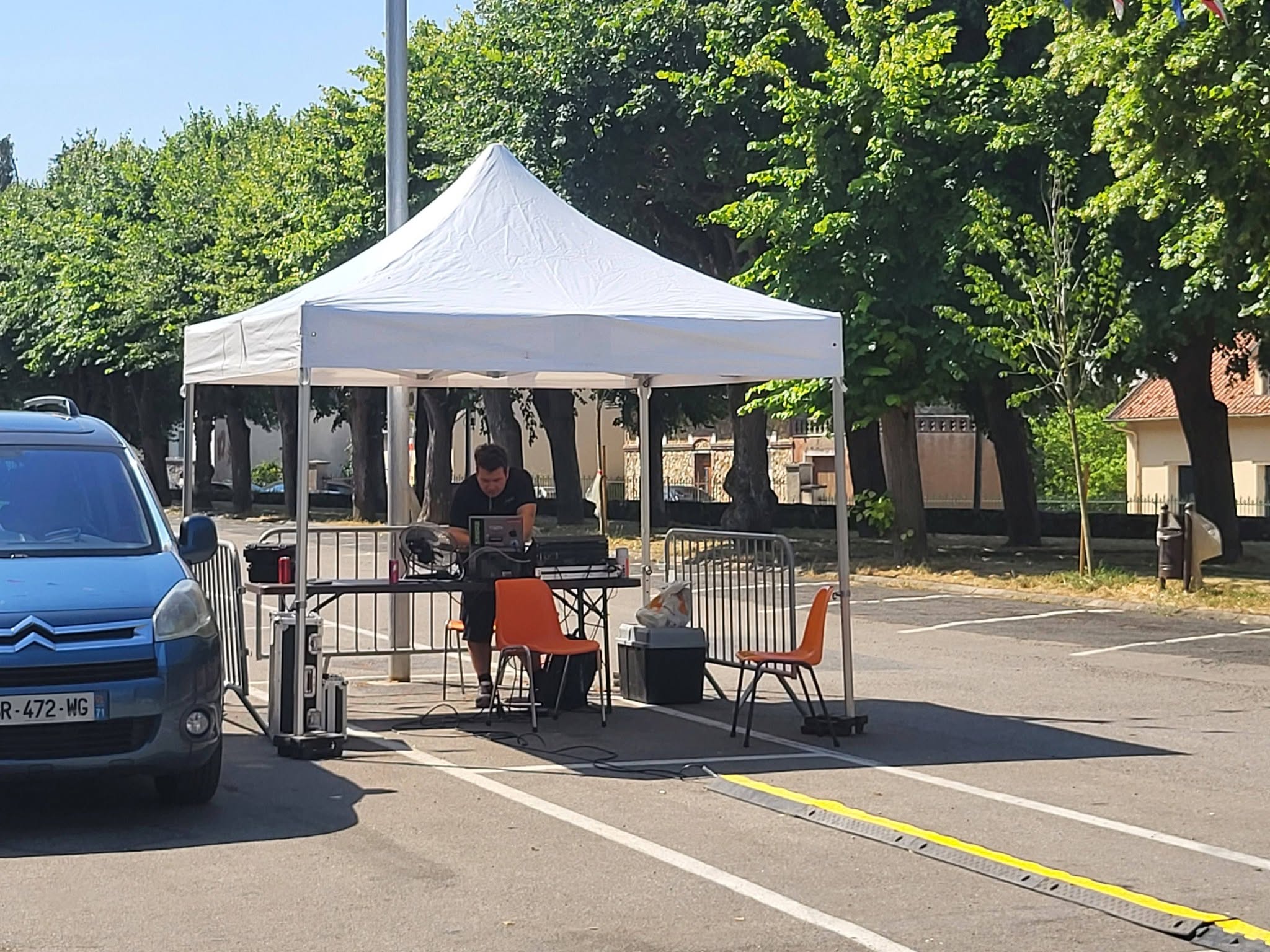 Installation de matériel de son et lumière sous un chapiteau avec un homme travaillant à un ordinateur dans un parking.